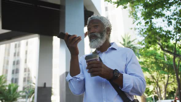 African american senior man drinking coffee and talking on smartphone in corporate park