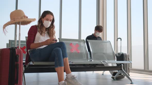 Man with hygiene mask bring suitcase go to sit on back row of waiting chair behind of woman