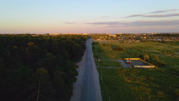 Aerial view over road towards sunlit houses and cars, in Shepetivka town, during golden hour, on the