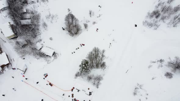 Happy Families Go Down the Hill in a Snowy Winter Park Aerial View From a Drone