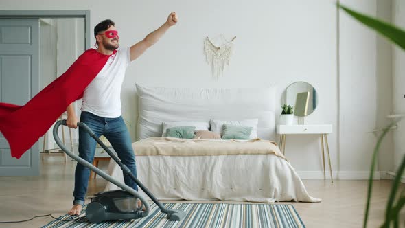 Superhero Wearing Red Cape and Mask Holding Vacuum Cleaner in Bedroom