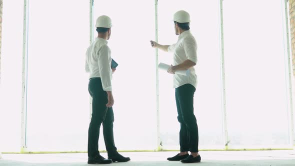 Two Engineer with a Drawing in Hand Looking at the Construction Site