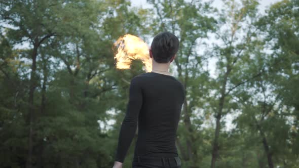 Young Slim Man in Black Clothes and Mask Performing a Show with Flame Standing on Riverbank