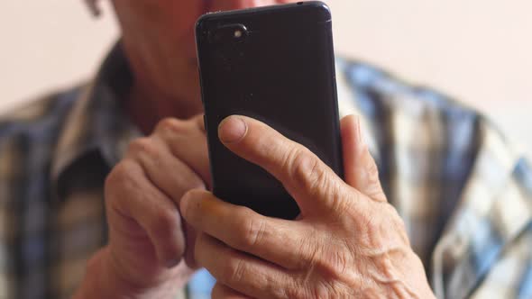 The pensioner holds a smartphone in front of him and presses the screen. An elderly man enjoys socia