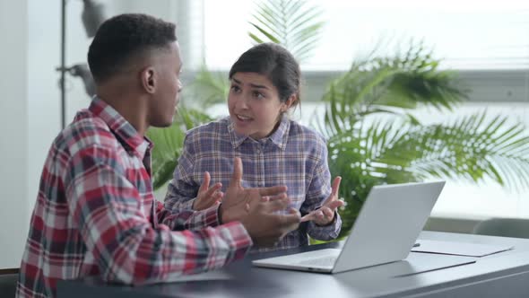 African Man and Indian Woman Arguing while Working on Laptop