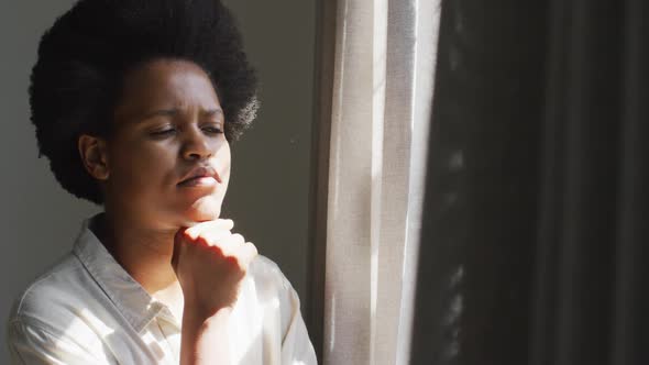 Thoughtful african american woman looking through window in bedroom