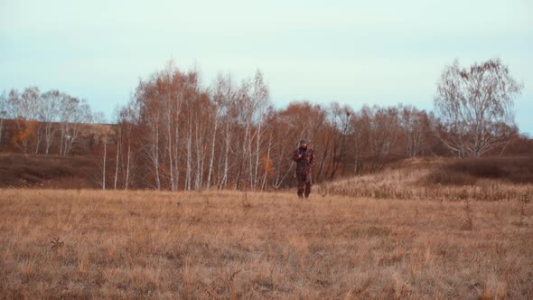 A Hunter with a Shotgun Walks Through an Autumn Field