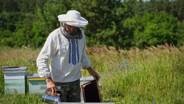 Beekeeper's work in summer. Professional apiarist working with chimney in the apiary among nature 