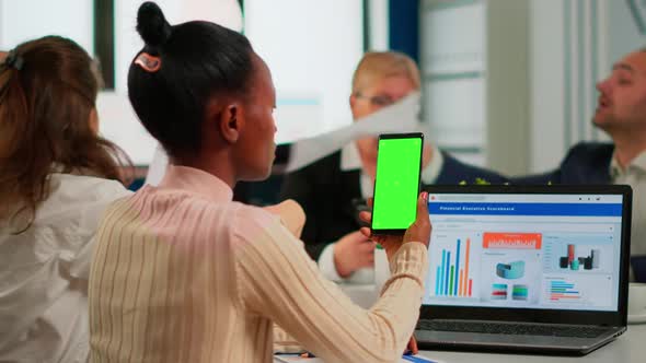 Black Businesswoman Sitting at Conference Desk Holding Smartphone with Green Screen