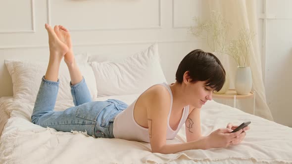 Relaxed woman with short hair lies at home on the bed and using a mobile phone