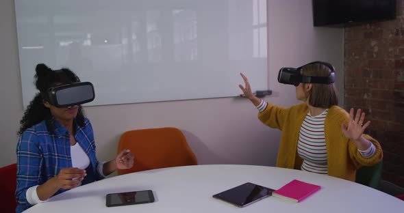 Diverse female business colleagues sitting at table using vr headsets in meeting room