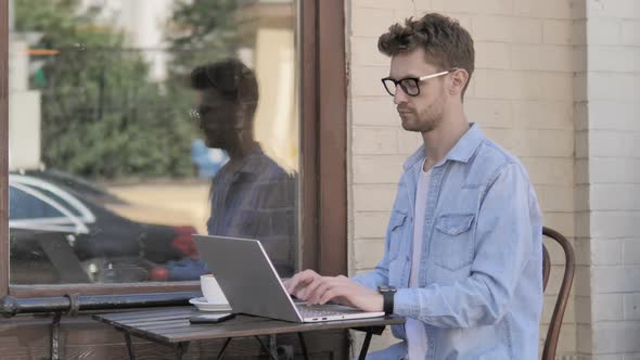 Young Man Sitting Outdoor and Using Laptop