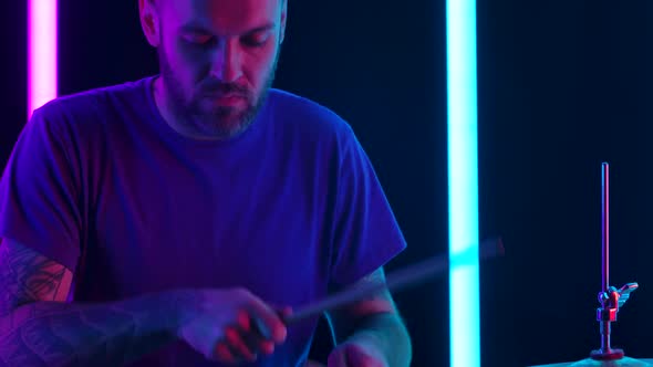Drummer Is Hitting Drum Cymbals with Drumsticks in a Dark Studio Against the Backdrop of Neon Tubes