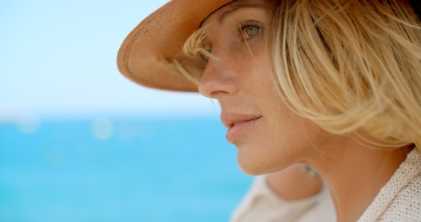 Blond Woman Wearing Hat In Front Of Blue Ocean