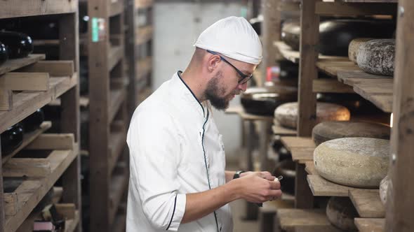 Side View Caucasian Cheese Maker in Eyeglasses Smelling Tasting Delicious Aged Cheese Standing at