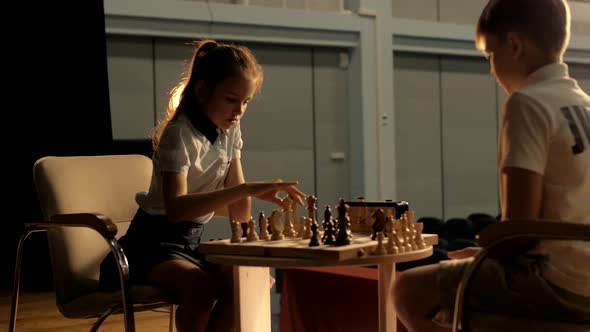 Beautiful cute schoolgirl playing chess with a classmate during the championship. Cinematic