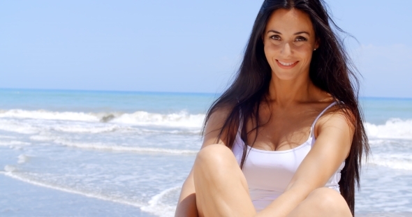 Brunette Woman Sitting In Sunshine On Beach alt