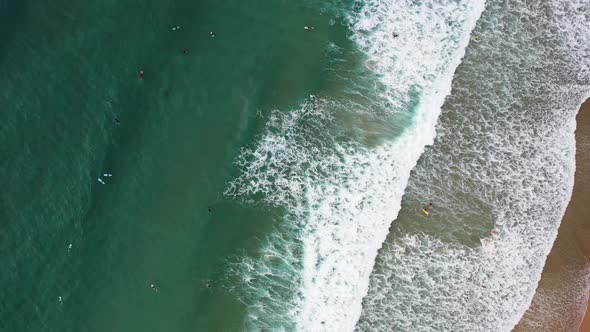Praia da Arrifana in west Portugal with Surfers seen from above riding waves, Aerial top view rotati