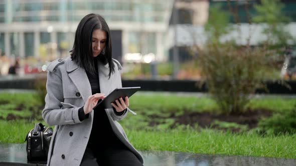 Modern Smart Lady is Checking Email or Working Chat By Tablet Sitting Outdoors in City