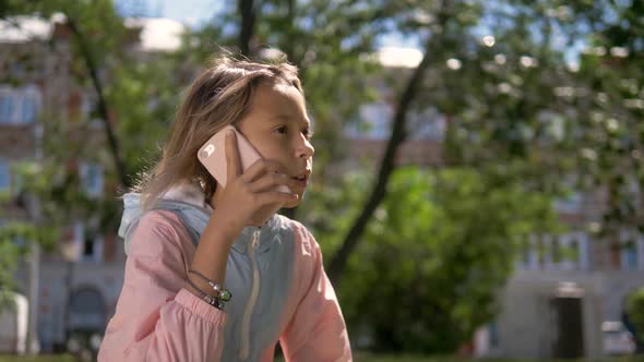 Beautiful Little Girl Is Talking on a Phone and Lying on a Green. Grass on a Sunny Summer Day