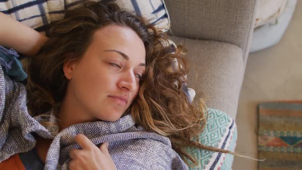 Caucasian woman lying on sofa with blanket, relaxing and looking away in cottage living room