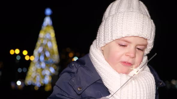 A Beautiful Christmas Child Plays with a Sparkler in Front of a Christmas Tree