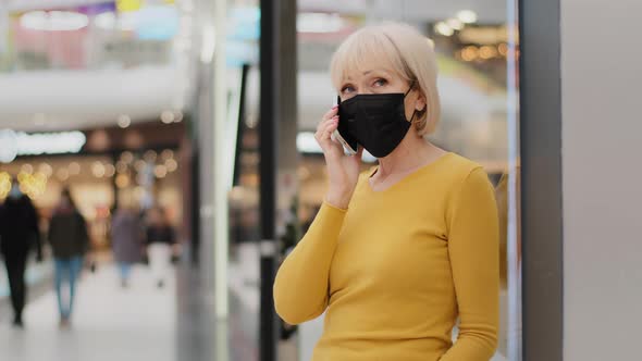 Mature Adult Caucasian Woman in Protective Mask Standing in Mall Talking on Phone Answering Mobile