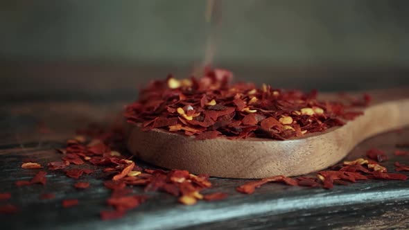 Flakes of Red Hot Chili Pepper in Wooden Spoon Closeup on a Kitchen Table.