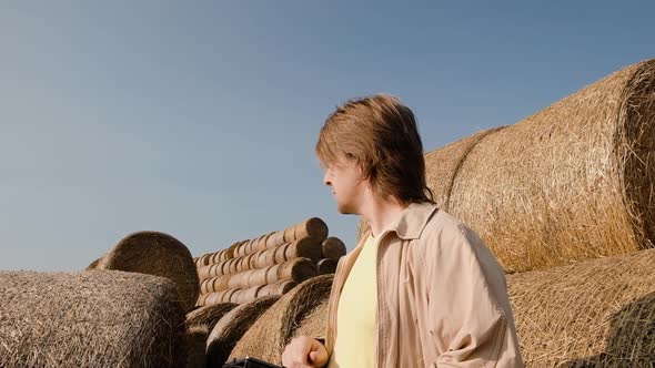 Farmer Agronomist Checks Hay Bales on the Wheat Field After Harvest at Sunset