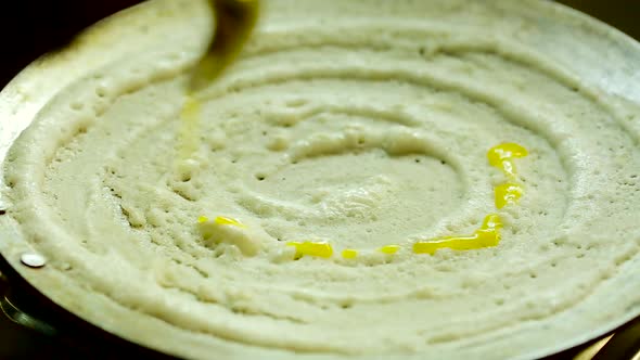 Time lapse shot of young Indian woman cooking dosa and pouring ghee on the dosa in home kitchen