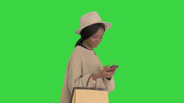 Happy African American Fashion Girl in Knitted Oversized Sweater and Hat Texting on Her Phone While