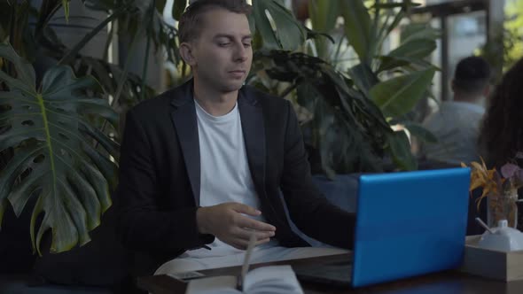 Focused Caucasian Businessman Using Smartphone and Laptop in Cafe. Portrait of Young Handsome Man