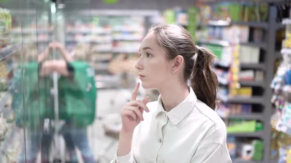 A Girl Shopper Looks at the Refrigerator with Food in the Supermarket