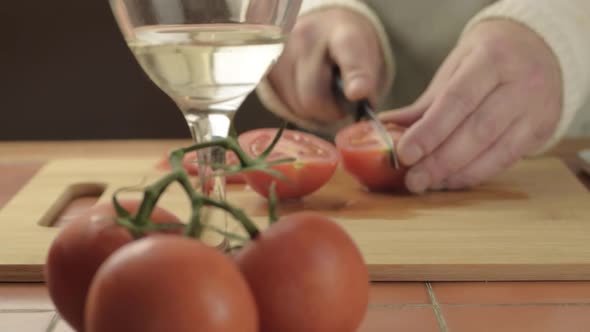 Hands cutting fresh vine tomatoes in kitchen with glass of white wine medium shot