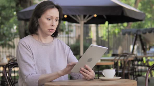 Upset Old Woman Reacting to Loss on Tablet in Outdoor Cafe