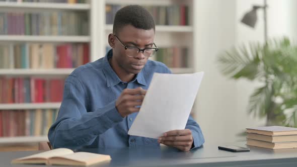 Young African Man Reading Reports While Sitting in Office