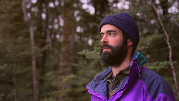 Young Man with Dark Beard and Winter Clothing Contemplating the Nature in the Lush Forest