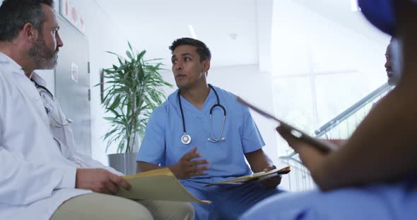 Mixed race male doctor sitting and discussing with diverse colleagues at hospital staff meeting