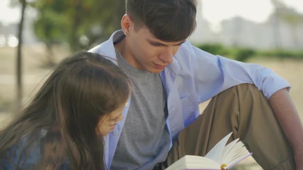 Portrait of Boy with His Small Sister Reading Book with Poems or Tales Sitting Outdoor in Park in