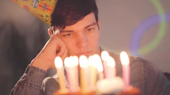 Lonely Sad Boy Sitting in Front of Little Cake with Lighted Candles Looking on It