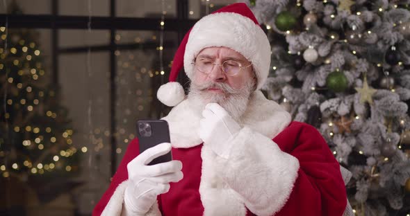 Brooding Santa Reads the Message on His Smartphone Strokes His Mustache and Looks Around Nodding His