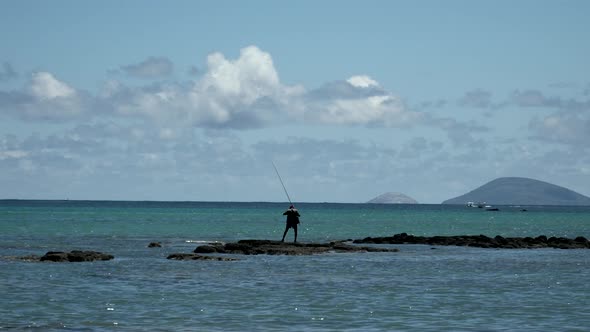 Fisherman standing on rock in ocean and angling fish with rud