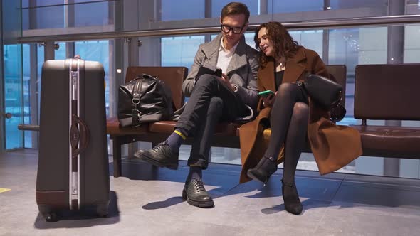 Portrait of Cheerful Man Speaking with Happy Female Using Digital Device While Locating in Airport