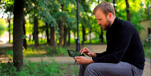 Man With the Tablet Computer on a Bench in a Park