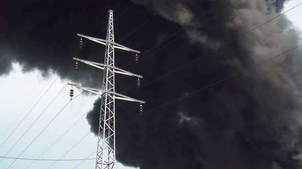 An Electric Tower Stands Against a Background of Black Smoke. A Big Chemical Fire at a Factory