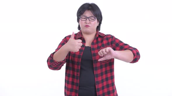 Confused Overweight Asian Hipster Woman Choosing Between Thumbs Up and Thumbs Down