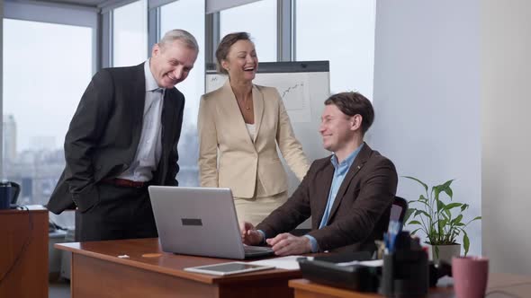 Joyful Laughing Colleagues Looking at Laptop Screen Talking in Office