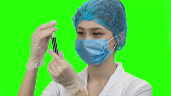 Young Female Doctor with Mask Looks at Blood Test Tube