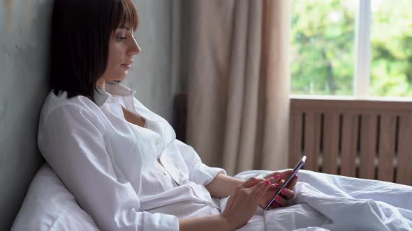 Overjoyed Young Latino Woman Relax in Bedroom Use Cellphone Texting or Messaging Online