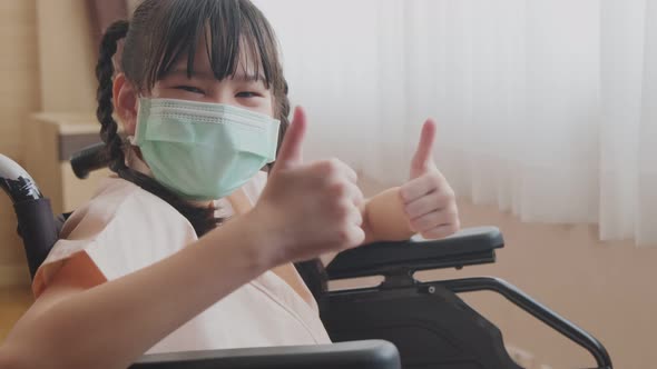 Asian little illness girl sitting on wheelchair and wearing face mask in hospital during the COVID19